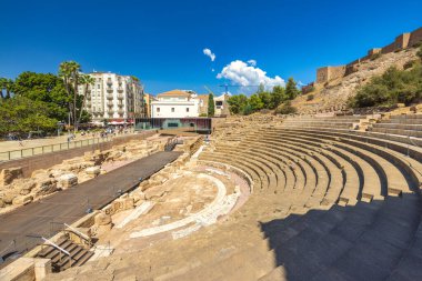 Malaga, İspanya - 11 Eylül 2024: Roma Tiyatrosu. Antik Roma amfitiyatro kalıntıları güneşli bir şehir ortamında. Modern binalarla çevrili tarihi bir yer..