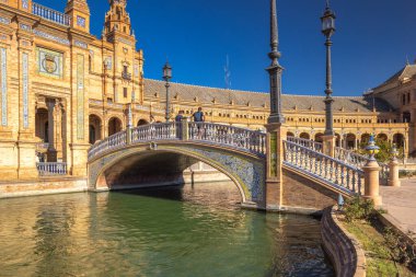 Seville, İspanya - 8 Eylül 2024: İspanya 'nın başkenti Endülüs' teki Plaza de Espana Meydanı. Kanal boyunca uzanan süslemeli köprü, arka planda büyük bir bina. Turistler köprüde yürüyor.