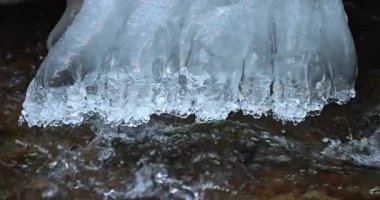 Büyüleyici donmuş şelale kristal berraklığında buz saçakları, sakin kış manzarasını yansıtıyor, altındaki yumuşak, akan nehre karşı yan yana geliyor..