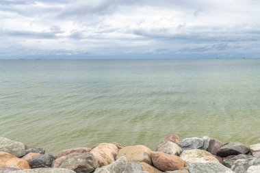 Kuzey Polonya 'da Baltık Denizi kıyısında. Sakin sular ufukta, kayalık kıyı şeridi ile çevrili bulutlu bir gökyüzünün altında uzanır. Sakin kıyı manzarası.
