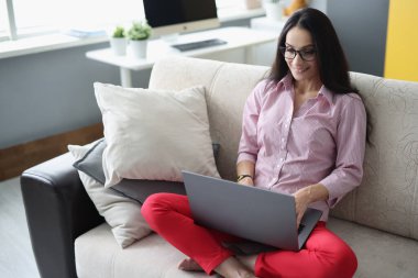 Gülümseyen kadın kanepede oturuyor ve bilgisayar başında çalışıyor..