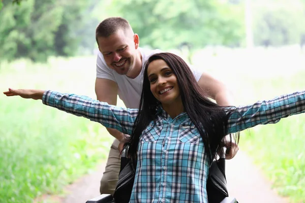 Kvinnan sitter i rullstol leende med armarna utspridda mannen rullar. — Stockfoto