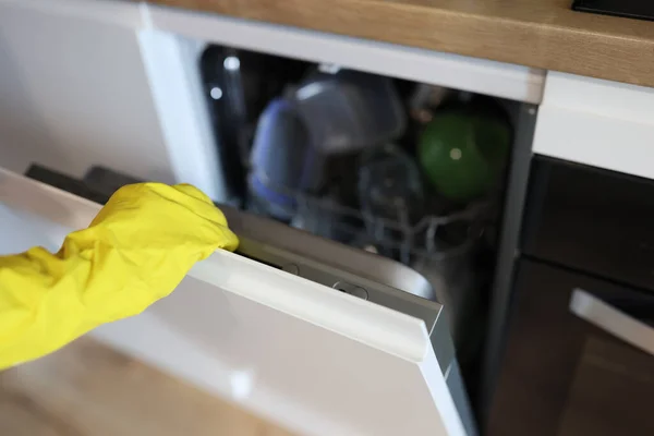 Hand in Hand mit gelbem Handschuh öffnet Spülmaschine in Großaufnahme — Stockfoto
