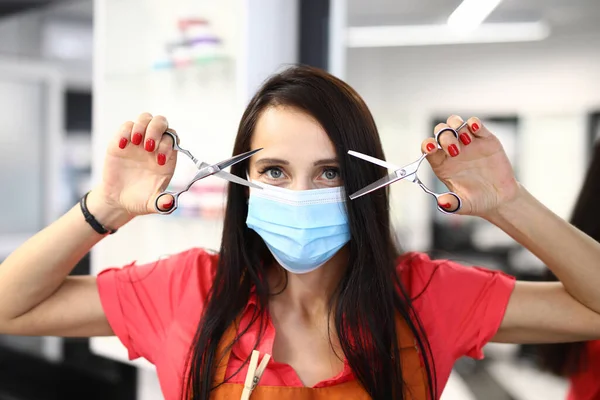 Peluquería en una máscara médica protectora sostiene tijeras para cortar el cabello. — Foto de Stock