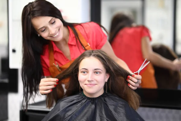 Uśmiechnięta kobieta mistrz fryzjer trzyma włosy klienta i nożyczki w rękach — Zdjęcie stockowe