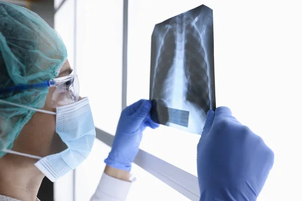 Femme médecin en masque médical de protection et des lunettes regarde une image de rayons X. — Photo