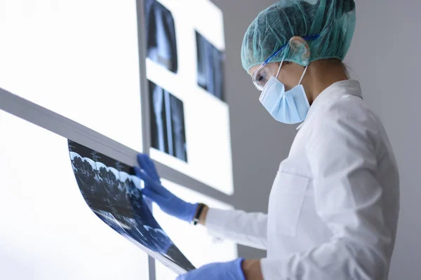 Médecin au bureau en masque médical de protection et des lunettes regarde l'image de rayons X. — Photo