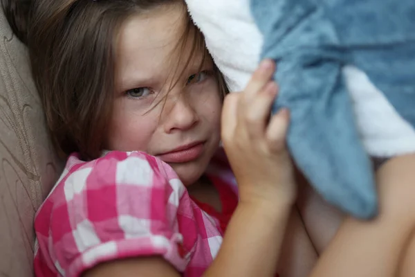 Little girl sits on sofa offended with soft toy. — Stock Photo, Image