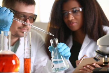 Laboratuvardaki bilim adamları şişeyi tutup içine temiz sıvı damlatıyorlar..
