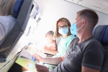 Kadın ve erkek uçakta oturuyorlar. Koruyucu maskeler takıyorlar.