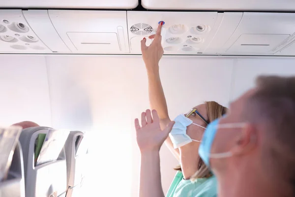 Mężczyzna i kobieta w ochronnych maskach medycznych naciśnij przycisk wywołania w samolocie. — Zdjęcie stockowe