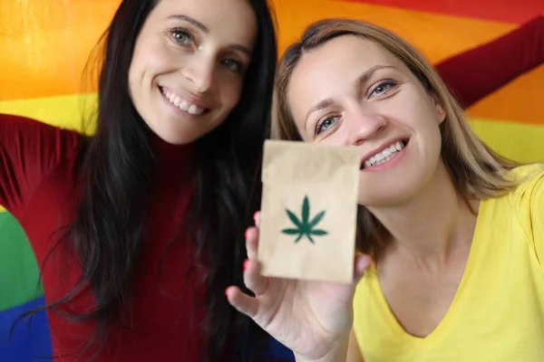 Duas mulheres estão segurando uma bandeira lgbt e saco de papel com sinal de maconha — Fotografia de Stock