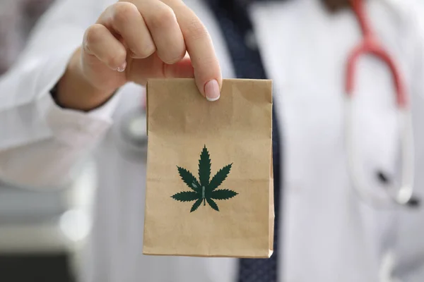 Orvos sztetoszkóppal a nyak körül tartja papírzacskó marihuána közelkép — Stock Fotó