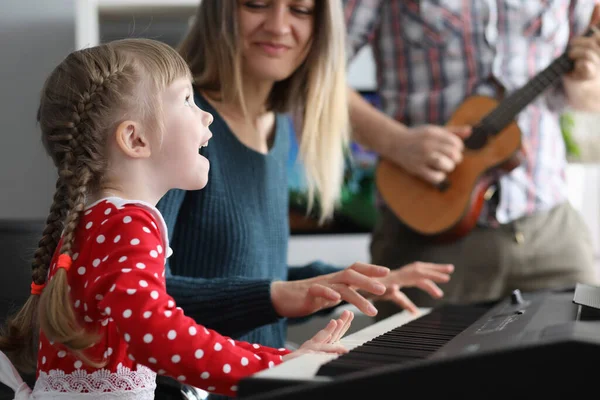 Pequena menina bonita canta música é tocada no piano, juntamente com seus pais retrato — Fotografia de Stock