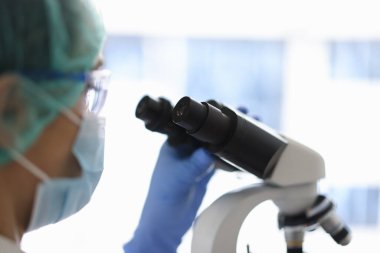 Gözlüklü doktor ve tıbbi maske mikroskoptan bakıyor..