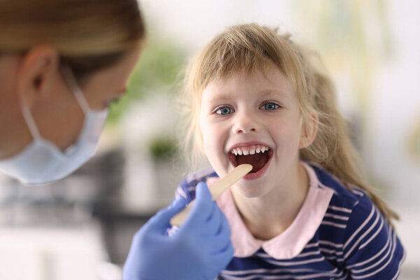 Doctor wearing protective mask examines throat of little girl
