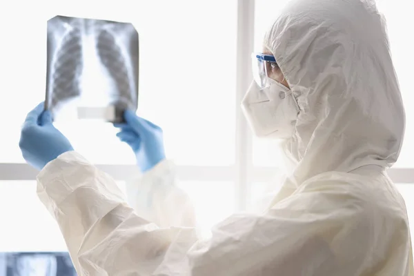 Médico en mono protector y respirador sostiene imagen de rayos X cerca de la pantalla en el hospital — Foto de Stock
