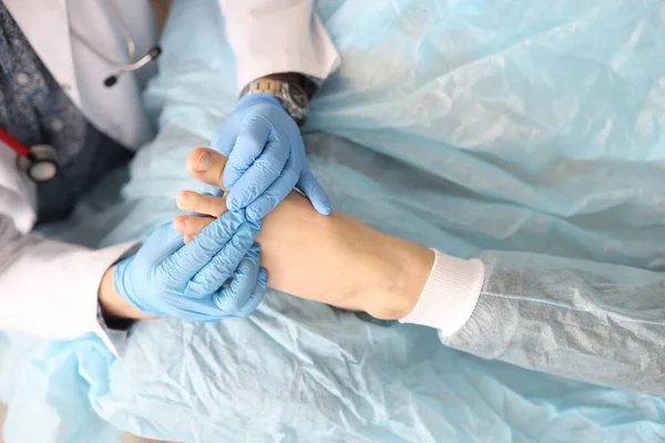 Dermatologista está segurando pé de mulher com o polegar danificado em suas mãos em luvas de borracha na clínica — Fotografia de Stock