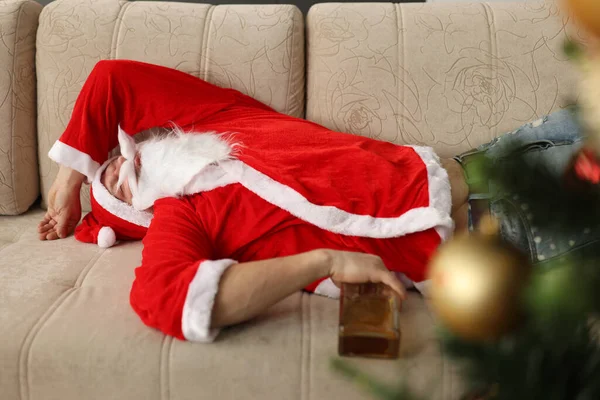 A részeg Télapó a kanapén alszik egy üveg whiskyvel a kezében otthon. — Stock Fotó