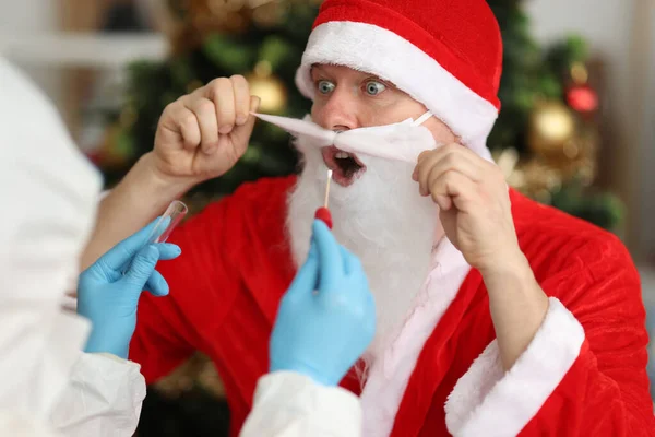 Доктор в защитном костюме берет мазок от Санта-Клауса возле елки — стоковое фото
