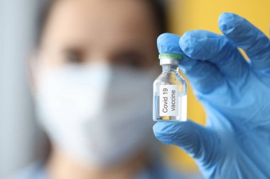 Koruyucu tıbbi maskeli bir doktor elinde kovid 19 aşısı olan bir şişe tutuyor.