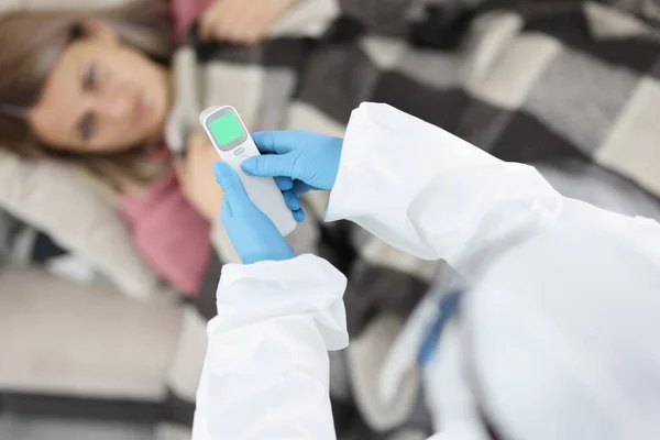 Arzt in Schutzanzügen und Gummihandschuhen hält Thermometer in der Nähe kranker Patient zu Hause — Stockfoto