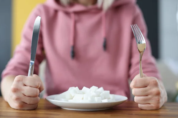 Vrouw met vork en mes in handen in de buurt plaat met klontjes suiker in de keuken — Stockfoto