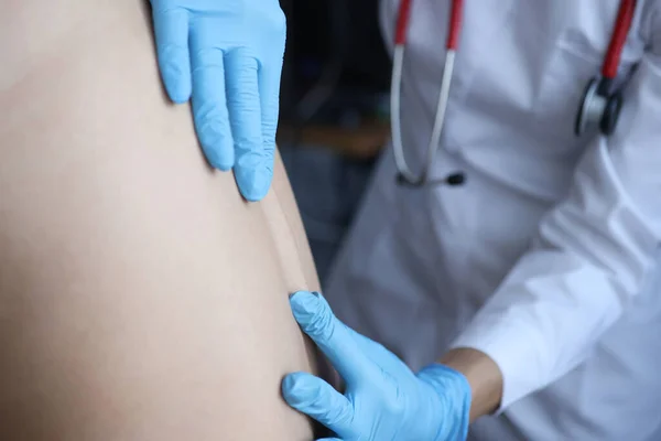 Doctor in rubber gloves palpating pain points near patients spine in clinic closeup