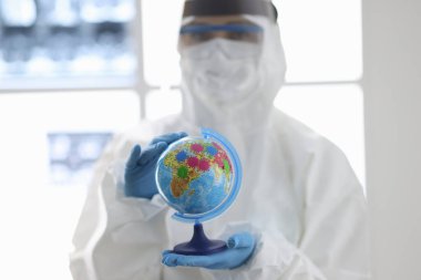 Koruyucu giysili ve maskeli doktor dünyayı elinde tutuyor.