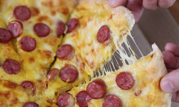 Male hands tearing off slice of pizza with cheese and sausage close-up — Stock Photo, Image