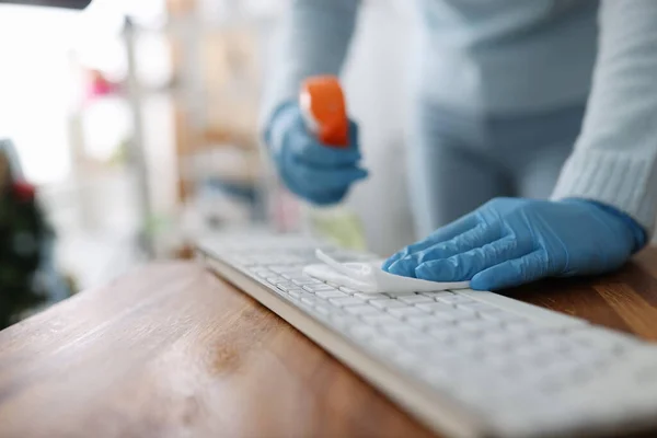 Female hands in rubber gloves wiping keyboard with antiseptic napkin in office