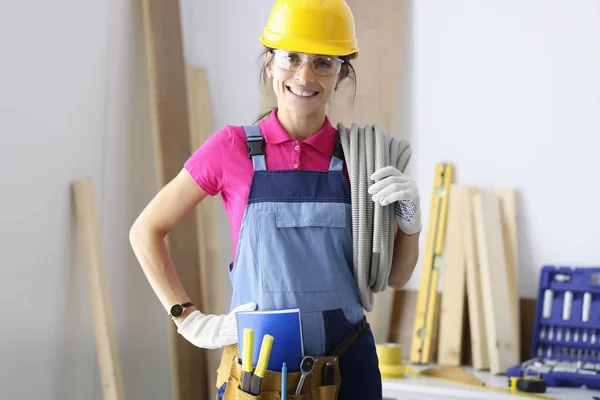 Vrouw met gele helm en overall met elektrische kabel op de schouder — Stockfoto