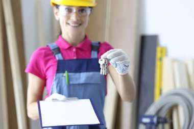 İnşaatçının elinde anahtarlar ve bir pano var..