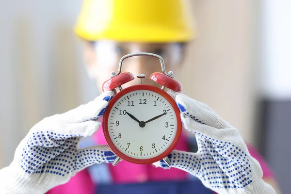 Builder holds red alarm clock in his hands.