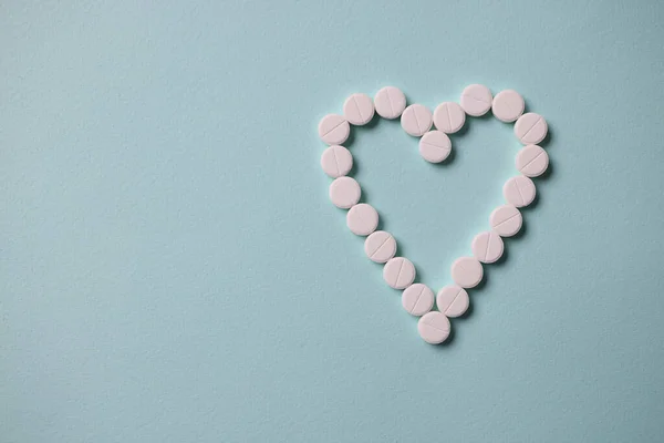 White tablets lying in shape of heart on blue background