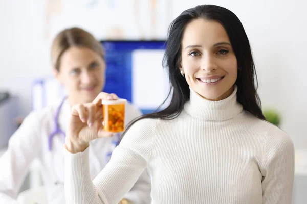 Mujer médico y paciente están sonriendo y sosteniendo frasco de píldoras — Foto de Stock