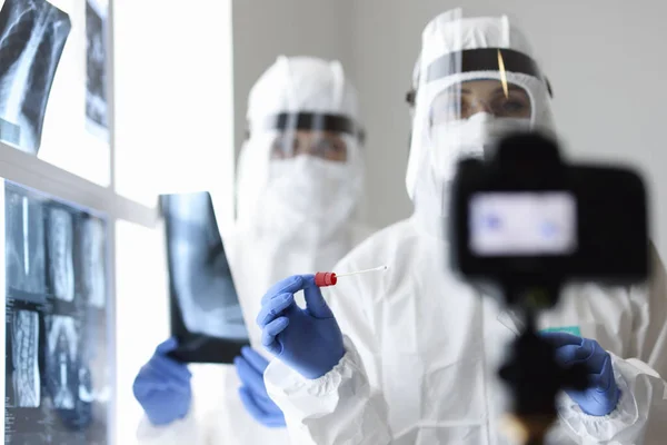 Två läkare i skyddsdräkter tar en röntgen med test för analys och skjuter den på kameran. — Stockfoto