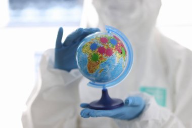 Koruyucu kıyafetli doktorun elleri küreyi tutuyor..
