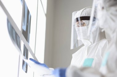 Koruyucu giysili ve maskeli iki doktor röntgenleri inceliyor..