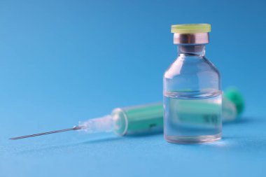 Klinikte mavi arka planda duran ilaç ve şırınga şişesi.