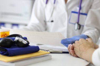 Eldivenlerle kardiyogramı tutan doktor ve klinikte hastaya yakın çekim tavsiyesi veren doktor.