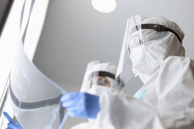 Koruyucu ekranlı ve veba önleyici giysili iki doktor klinikteki röntgene bakıyorlar.