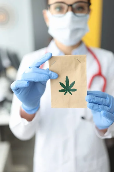 Doctor en guantes de goma sosteniendo bolsa de papel con marihuana en primer plano clínica — Foto de Stock