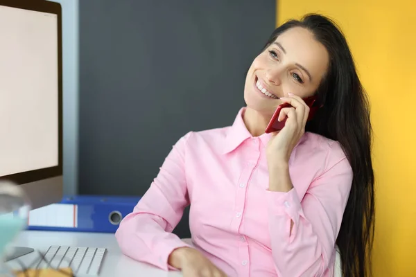 Joven mujer sonriente hablando en el teléfono celular en la mesa en la oficina — Foto de Stock