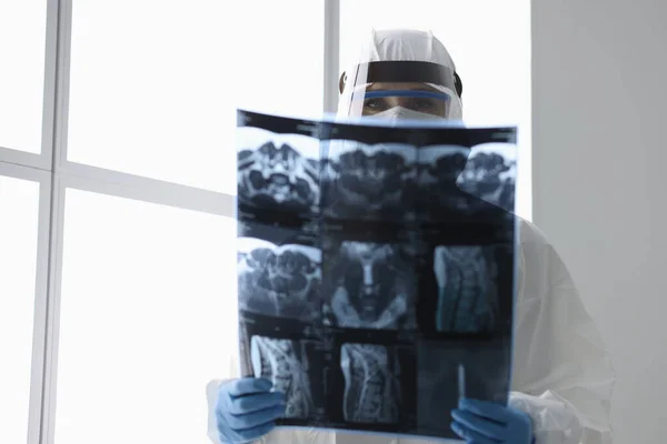 Médico en traje protector que sostiene la imagen de rayos X en la clínica —  Fotos de Stock