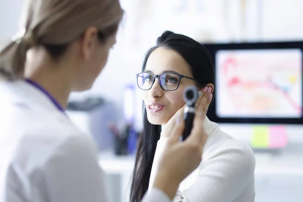 Woman patient holding ear near doctor with otoscope in hand in clinic — Stock Photo, Image