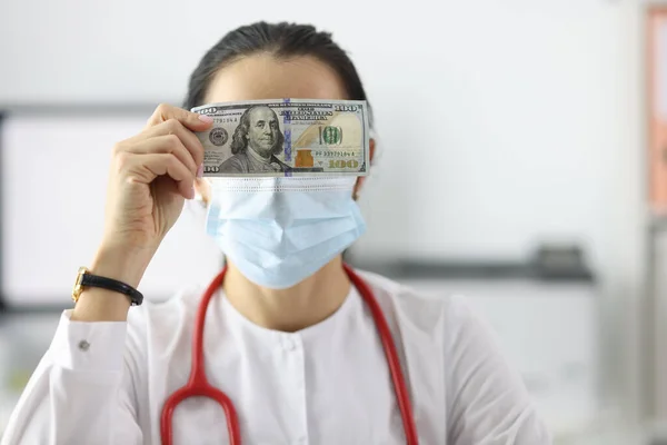 Doctor holding dollar bill near his eyes in clinic closeup