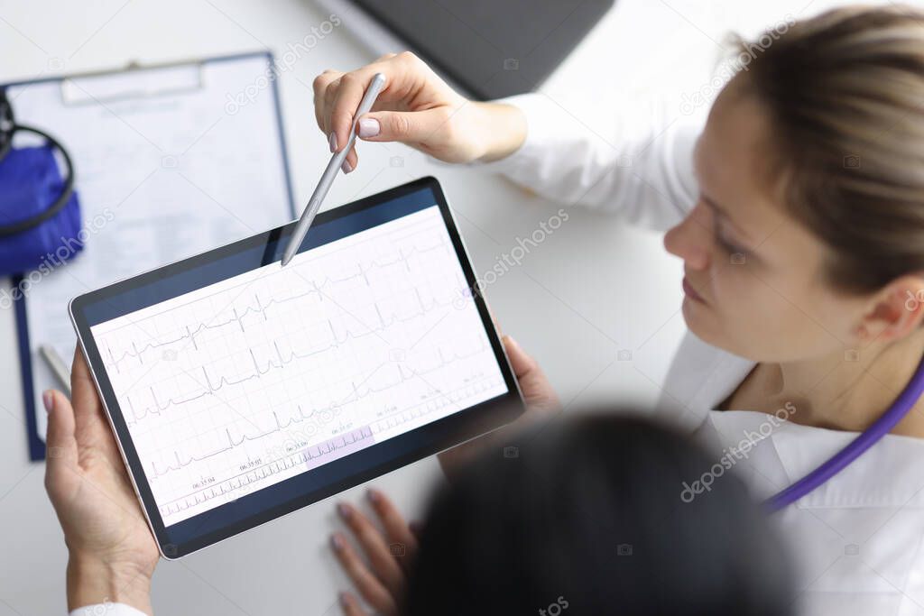 Doctors cardiologists looking at cardiogram on tablet and showing it with pen