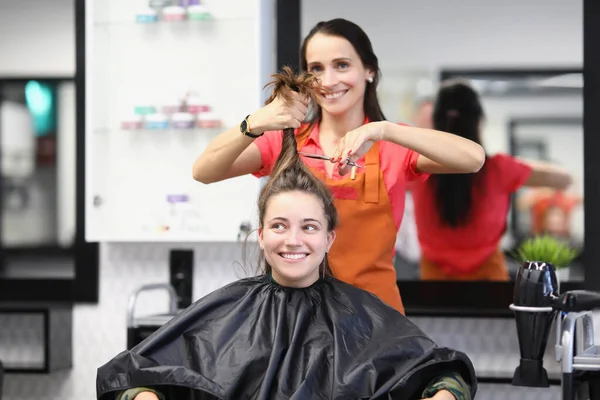 Il parrucchiere tiene la coda di cavallo di capelli in mano in cima e taglia capelli corti con forbici in studio. — Foto Stock