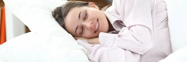 Счастливая девушка в пижаме лежит в постели и закрывает глаза. — стоковое фото